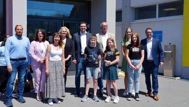 Gruppenfoto von Erwachsenen und Schülerinnen und Schülern vor dem Schuleingang, ein T-Shirt mit Aufschrift „SOR SMC“