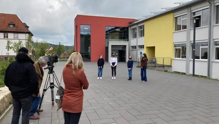 Kamerateam filmt vier Schülerinnen und Schüler vor dem Schulgebäude