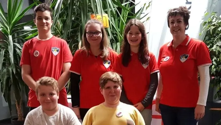 Fünf Jugendliche und eine Frau in roten Poloshirts mit Schullogo vor Pflanzen