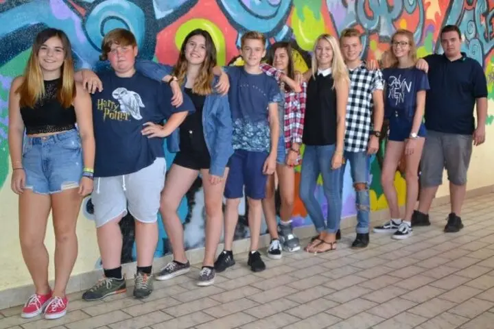 Gruppe Jugendlicher steht Arm in Arm vor einer bunt bemalten Wand