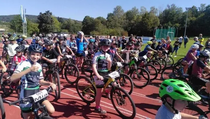 Viele Jugendliche mit Helmen und Mountainbikes auf einer Laufbahn vor dem Start