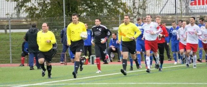 Schiedsrichter in gelben Trikots laufen mit zwei Fußballmannschaften aufs Spielfeld