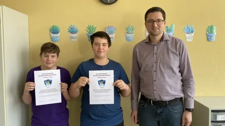 Zwei Schüler halten Urkunden „Schülervorbild des Monats Februar 2024“, daneben ein Erwachsener