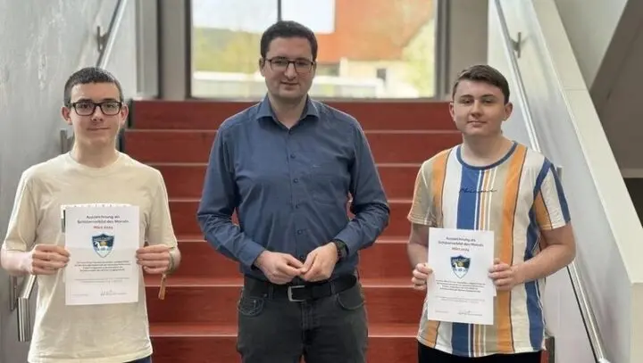 Zwei Schüler mit Urkunden „Schülervorbild des Monats März 2024“ und ein Erwachsener auf einer Treppe