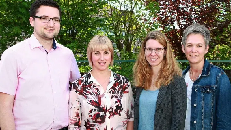 Gruppenfoto von vier Erwachsenen im Freien vor grünen Bäumen