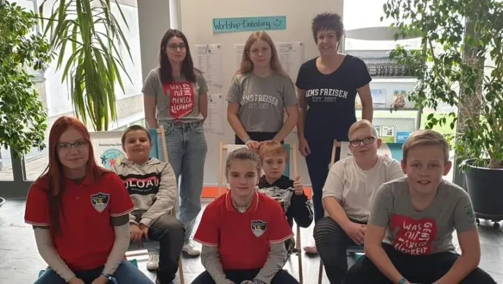 Gruppenbild der Schulsanis, teils in roten Poloshirts, vor einer Wand mit der Aufschrift „Workshop-Einteilung“