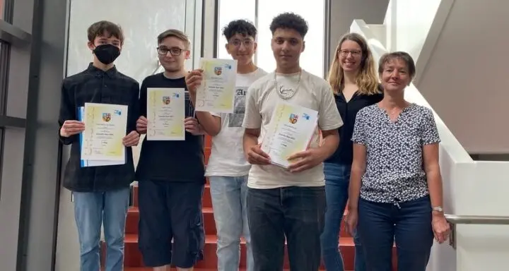 Vier Schüler halten auf einer Treppe ihre Urkunden hoch, daneben zwei Erwachsene