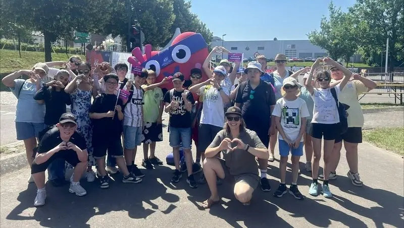 Klassengruppe formt Herzen mit den Händen vor einer Maskottchen-Figur im Freien