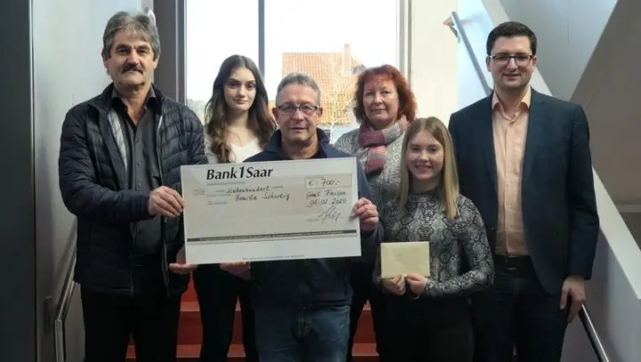 Sechs Personen halten einen Spendenscheck der Bank 1 Saar über 700 Euro, eine Jugendliche hält einen Umschlag