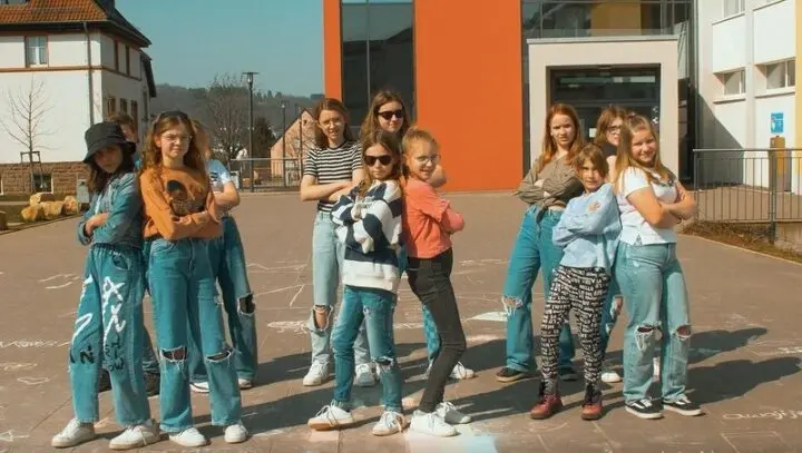Gruppe Jugendlicher posiert mit verschränkten Armen auf dem Schulhof vor dem Schulgebäude