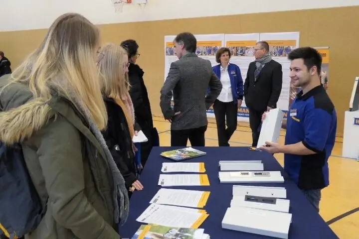 Schülerinnen informieren sich an einem Firmenstand mit Broschüren und Produktmustern in der Turnhalle
