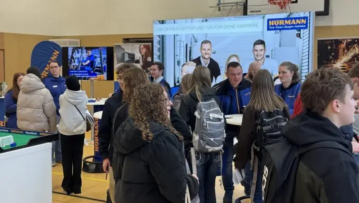 Schülerinnen und Schüler mit Rucksäcken an einem Informationsstand der Firma Hörmann in der Turnhalle