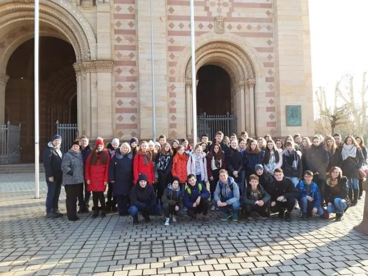 Große Gruppe von Jugendlichen und Erwachsenen in Winterkleidung vor dem Portal eines romanischen Doms