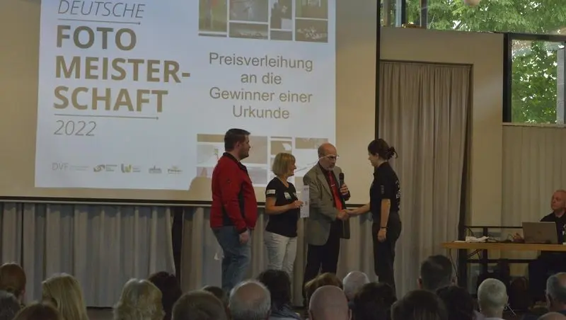 Übergabe einer Urkunde auf der Bühne vor der Leinwand „Deutsche Fotomeisterschaft 2022 – Preisverleihung“