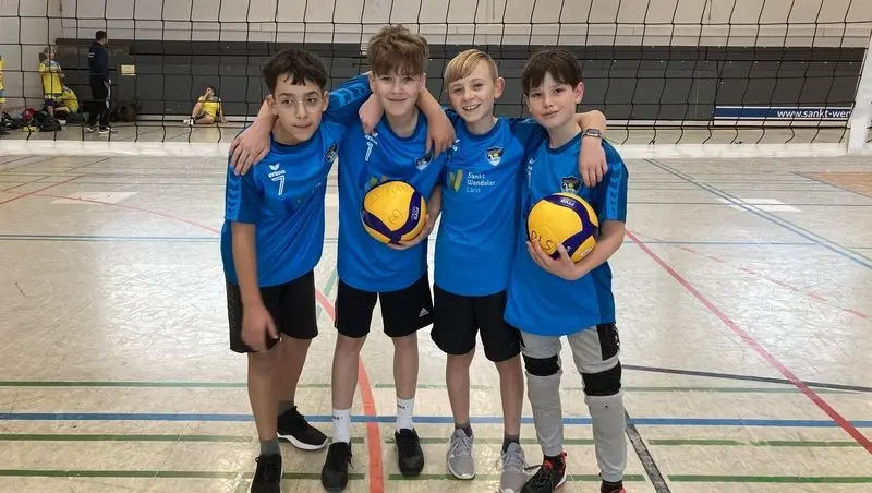Vier Jungen in blauen Volleyballtrikots mit zwei Bällen in der Sporthalle