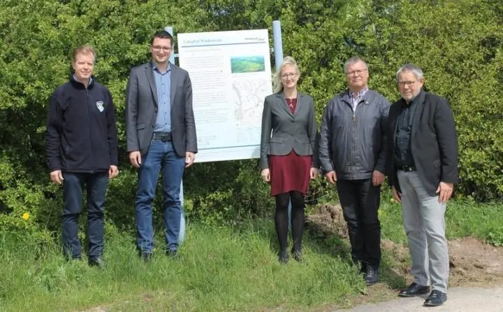 Fünf Erwachsene stehen auf einer Wiese neben einer Infotafel zum Lehrpfad Windenergie