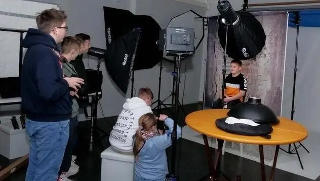Jugendliche fotografieren in einem Fotostudio mit Blitzschirmen einen Jungen am Tisch