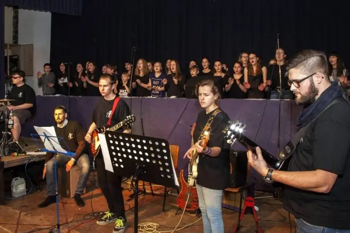 Band mit Gitarren und Cajón spielt vor dem singenden Chor auf der Bühne
